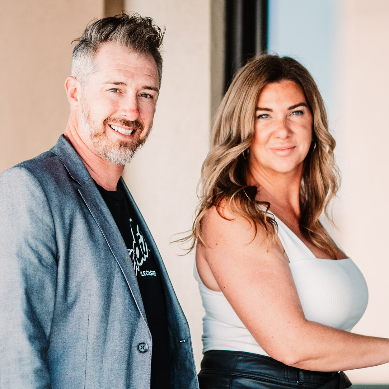 Define Hair & Skin in Ellicott City, MD A man in a grey blazer and a woman in a white top stand together, both looking at the camera and smiling, representing Our Team.